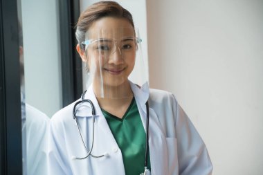 Asyalı kadın doktorlar virüslerden korunmak için yüz koruyucu takarlar. Hastanenin penceresinden. Hastane personeli kavramı.