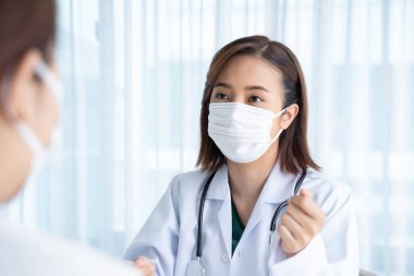 Doktor muayene odasındaki hastaların semptomlarını soruyor..