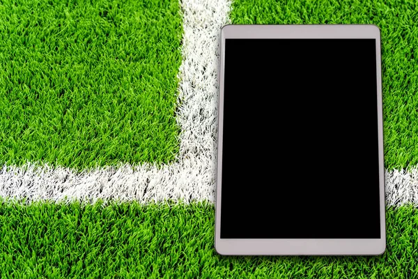 Digital tablet on green artificial grass soccer field background.