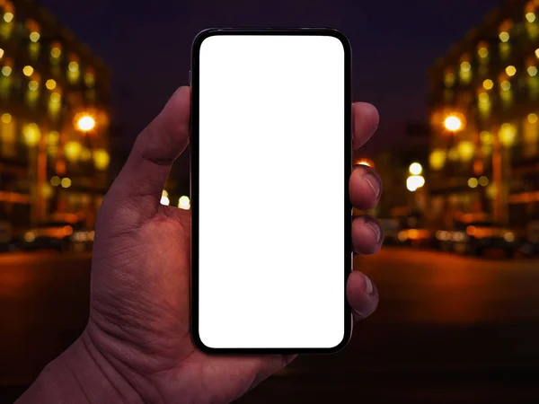 都市の夜の明るい背景の抽象的なボケ味を持つスマート フォンを持っている手 — ストック写真