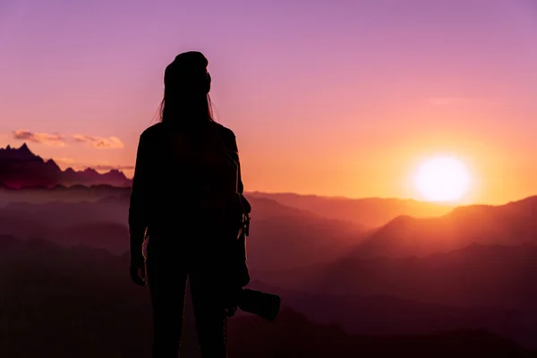 Back view of young hipster photographer holding the camera with sunset on mountain natural background.