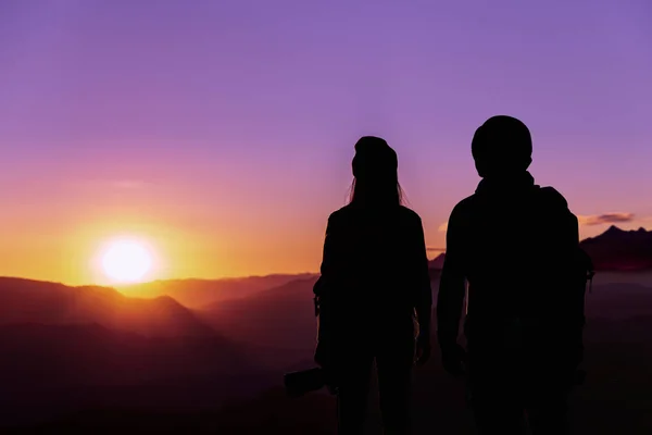 Back view of young hipster photographer holding the camera with sunset on mountain natural background.