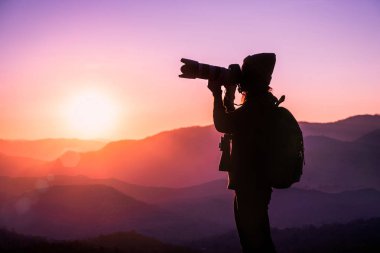 Genç hipster kadın fotoğrafçı alarak fotoğraf dağ doğal zemin üzerine gün batımı ile.