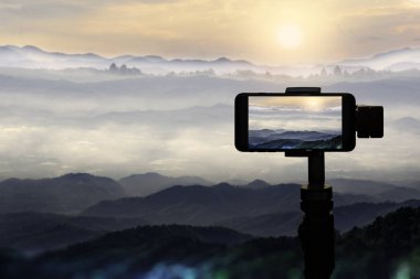 Bir gün batımı dağlar doğal arka plan fotoğrafta üçayağa Smartphone kullanarak gezgin.
