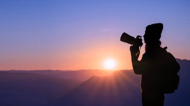 Genç hipster kadın fotoğrafçı alarak fotoğraf dağ doğal zemin üzerine gün batımı ile.