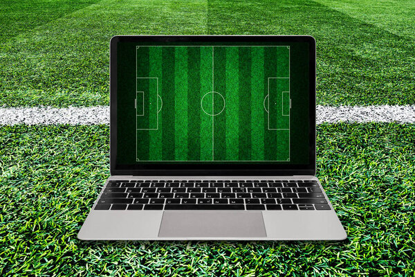 Laptop on green grass soccer field background.