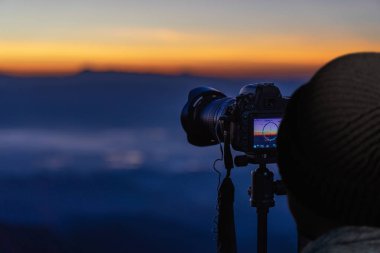 Gün batımında dağ manzarasının fotoğraflarını çeken gezgin fotoğrafçı.