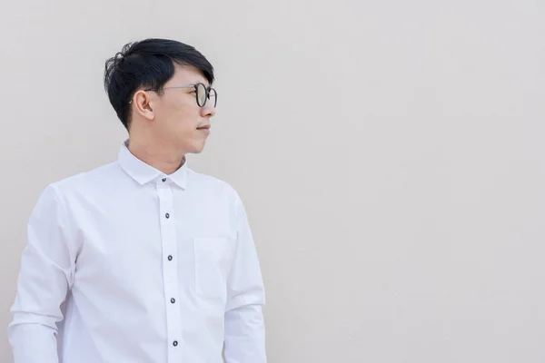 Side portrait of asian guy in white shirt on wall background.