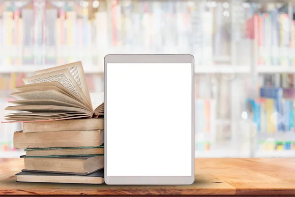 Boeken en Tablet PC op houten tafel met vervaagde veel boeken in bibliotheek achtergrond. — Stockfoto