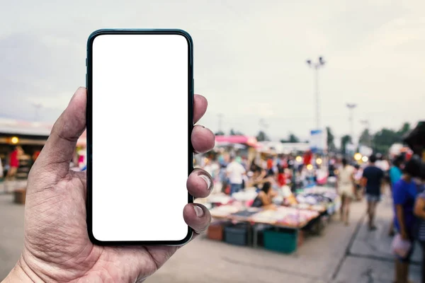 Рука держит смартфон с размытыми туристами ходить по ночному рынку . — стоковое фото
