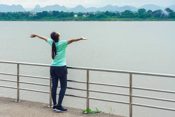 Mulher é relaxar de pé após correr com vista para o rio pela manhã. — Fotografia de Stock