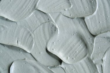 Gri kozmetik kil (kaolin, yüz kremi, maskesi, bodur) doku yakın kadar seçici odak. Fırça darbeleri ile arka plan. 