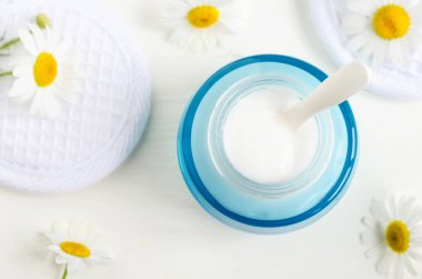 Mavi ışıklı cam kavanoz beyaz yüz kremi/maske ile. Yoğurt güzellik bakımı. hamomile çiçek beyaz arka plan üzerinde. Üstten görünüm, kopya alanı.  