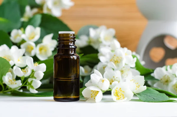 Small bottle of essential jasmine oil. Jasmine blossom flowers background. Copy space.