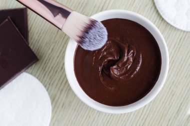 Küçük beyaz kase DIY kakao (bitter çikolata) ile yüz maskesi. Ev yapımı güzellik bakımı. Üstten görünüm, kopya alanı. 