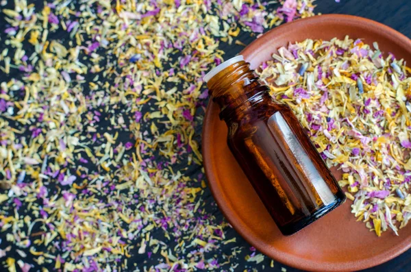 Petite bouteille à l'huile essentielle sur la petite assiette aux herbes et fleurs sèches. Fond avec des pétales de fleurs séchées. Concept aromathérapie, spa et phytothérapie. Espace de copie, vue du dessus . — Photo