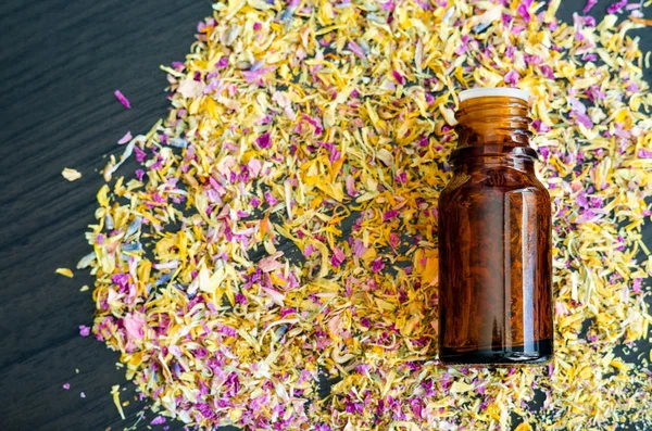 Small bottle with essential oil and dry herbs and flowers. Background with colorful dried flowers petals. Aromatherapy, spa and herbal medicine concept. Copy space, top view.
