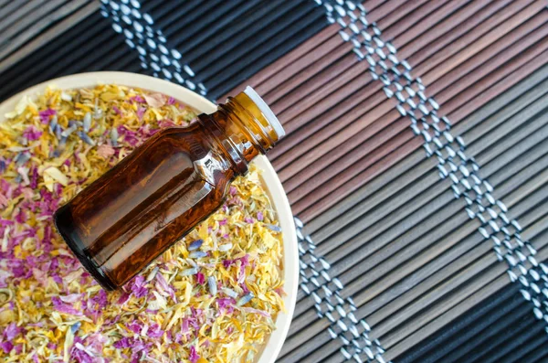 Botol kecil dengan minyak esensial di piring kecil dengan herbal kering berwarna-warni dan bunga. Latar belakang tikar bambu. Aromaterapi, spa dan konsep pengobatan herbal. Salin ruang, tampilan atas . — Stok Foto