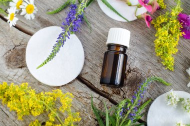 Uçucu yağ (tentür, infüzyon) ve pamuk ped ile küçük şişe. Aromaterapi ve doğal cilt bakım konsepti. Alan çiçekleri ile eski ahşap arka plan. Üst görünüm, kopyalama alanı. 