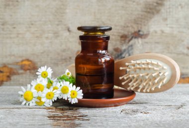 Roma papatya uçucu yağ (ekstre, tentür, infüzyon) ve ahşap saç fırçası ile Eczane şişe. Eski ahşap arka plan. Aromaterapi, doğal saç bakımı, spa, bitkisel ilaç kavramı. Kopyalama alanı 