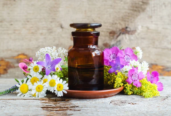 Bottiglia farmacia e vari fiori selvatici. Tintura di erbe (olio essenziale, infusione, estratto, sciroppo, composto). Vecchio sfondo in legno. Concetto di aromaterapia, spa e fitoterapia. Copia spazio . — Foto Stock