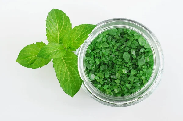 Sal de baño de aroma verde (remojo de pies) en un frasco de vidrio y hojas de menta. Tratamientos de belleza natural. Vista superior . — Foto de Stock