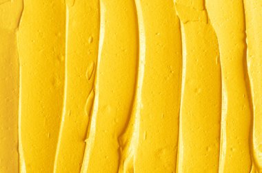 Sarı kozmetik yüz maskesi (krem, vücut scrub) doku yakın kadar seçici odak. Fırça darbeleri ile arka plan.  