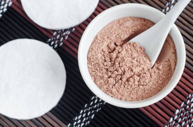 Küçük beyaz kâse ve pamuk pedlerde pembe bentonit kil tozu. Çamur dokusu yakın. Yüz veya saç maskesi, kuru şampuan tarifi. Doğal güzellik tedavisi ve spa. Üst görünüm, alanı kopyala
