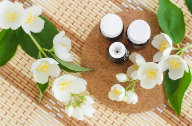 Beyaz zemin üzerinde yasemin yağı (tentür, infüzyon, parfüm) bulunan üç küçük cam şişe. Yasemin çiçekleri kapanıyor. Aromaterapi, spa ve bitkisel ilaç malzemeleri. Tip görünümü, kopyalama alanı.