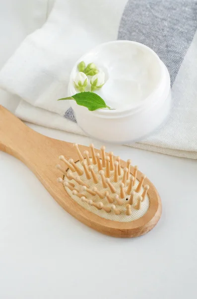 White hair mask (face cream or mask, body butter, facial cleanser) in the white jar and wooden hair brush. Natural skin and hair treatment concept. Copy space.