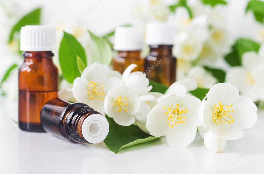 Small glass bottle with essential jasmine oil (tincture, infusion, perfume) on the white background. Jasmine flowers close up. Aromatherapy, spa and herbal medicine ingredients. Copy space. 
