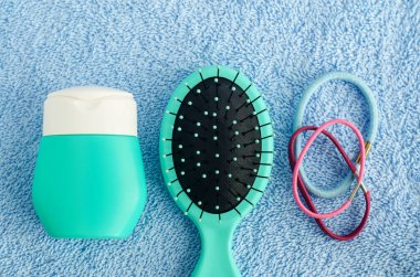 Saç şampuanı (maske, saç kremi, yüz kremi, güneş kremi), saç fırçası ve mavi havluda üç saç tokası. Üst görünüm, düz görünüm, kopyalama alanı. 