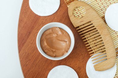 Küçük beyaz kasede kırmızı bentonit kil ve ahşap saç tarağı. Yüz maskesi, saç maskesi, vücut sarma tarifi. Doğal güzellik tedavisi ve spa. Üst görünüm 