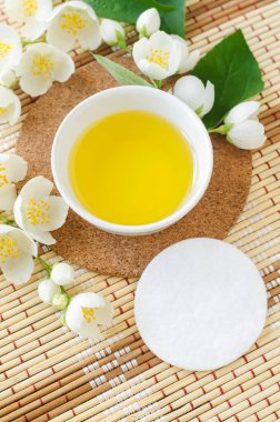 Kozmetik kaplı küçük beyaz kase (masaj, temizlik) aroma yağı, pamuk ped ve beyaz yasemin çiçekleri. Doğal cilt bakımı, ev yapımı spa ve güzellik tedavi tarifi. Üst görünüm, alanı kopyala. 