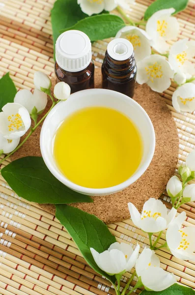 Small white bowl with cosmetic (massage, cleansing) aroma oil, small bottles with essential oil and white jasmine flowers. Natural spa and beauty treatment recipe. Top view, copy space.