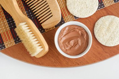 Küçük beyaz kasede kırmızı bentonit kil, lif süngeri masaj vücut fırçası ve ahşap saç tarağı. Yüz maskesi, saç maskesi, vücut sarma tarifi. Doğal güzellik tedavisi ve spa. Üst görünüm, alanı kopyala 