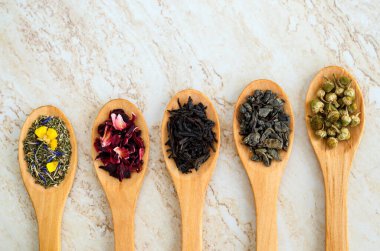 Beş tahta kaşık ve çeşitli çay çeşitleri. Siyah çay, yeşil çay, papatya çayı, amber çiçeği ve bitki çayı sağlıklı yaşam tarzı ve tıbbi amaçlar için. Doğal cilt bakımı ve bitkisel ilaç malzemeleri. Üst görünüm, alanı kopyala