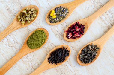 Altı tahta kaşık siyah çay, yeşil çay, kibrit, papatya, amber çiçeği sağlıklı yaşam tarzı ve tıbbi amaçlar için bitki çayı. Doğal cilt bakımı, bitkisel ilaç malzemeleri. Üst görünüm, alanı kopyala  