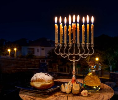 Bayram kompozisyonu, menorah mumlu fener, zeytinyağlı kavanoz ve gece karanlığında tatlı çörekler.