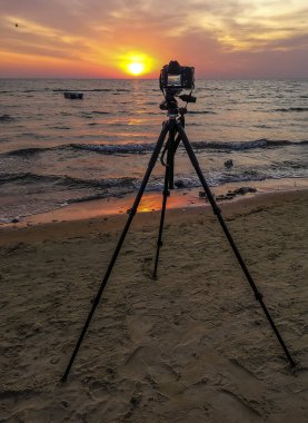 Baltık Denizi 'nin kumlu sahilinde gün doğumunda ön planda tripod ve fotoğraf makinesi olacak.