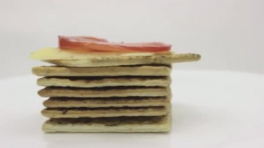 Bir yığın kraker, peynirli tost ve domates beyaz arka planda dönüyor.