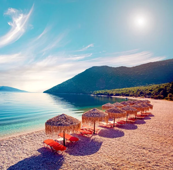 Fabulous beautiful magic landscape with umbrellas and orange sun beds on the seafront on Antisamos Beach on a sunny day on the coast of the Ionian Sea in Kefalonia, Greece. Amazing places. Tourist Attractions.
