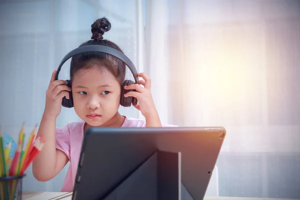 Technology plays an important necessary for communication. Kids in modern times need distance education online at home. Asian kid wearing headphones use a tablet learning with a teacher by video call.