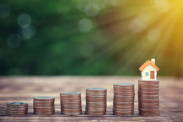 Yığınla para basan modern küçük ev arka plandaki ahşap masada üst tarafında fotokopi alanı olan yeşil doğada daha yüksek bir seviyeye yerleştirildi. Finansal, iş büyümesi, para kavramı.