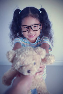 Asyalı sevimli kız gözlüklü portre takıyor. Elinde beyaz arka planda kahverengi bir oyuncak ayı var..