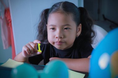 Yeni sosyal normallik. Küçük çocuk eğitim sosyal mesafesini öğreniyor. Asyalı kız öğretmene göstermek için cevap numaralarını alıyor. Yeni normal kavram, sosyal uzaklık, kendini izolasyon.