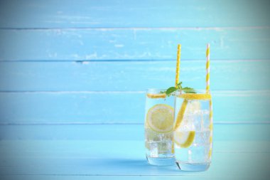 Yaz tatili. Meyve içecekleri. Limon suyu, alkolsüz soda ve mavi ahşap arka plandaki bardakta kaydırak limonuyla fotokopi alanı karışımı. Bu yaz sağlığa içelim..