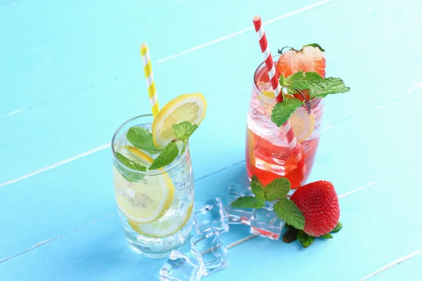 Lemon juice and strawberry juice mixing soda no alcohol in the glass garnish with mint leaves, sliced lime on blue wooden table with copy space. Concept of summer drink.