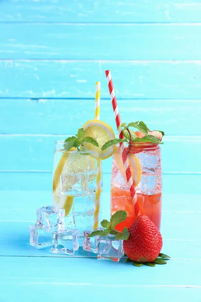 Strawberry juice and lemon juice mixing soda no alcohol in the glass garnish with mint leaves, sliced lime on blue wooden table with copy space. Concept of summer drink.