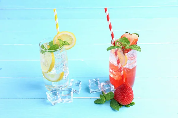 Lemon juice and strawberry juice mixing soda no alcohol in the glass garnish with mint leaves, sliced lime on blue wooden table with copy space. Concept of summer drink.